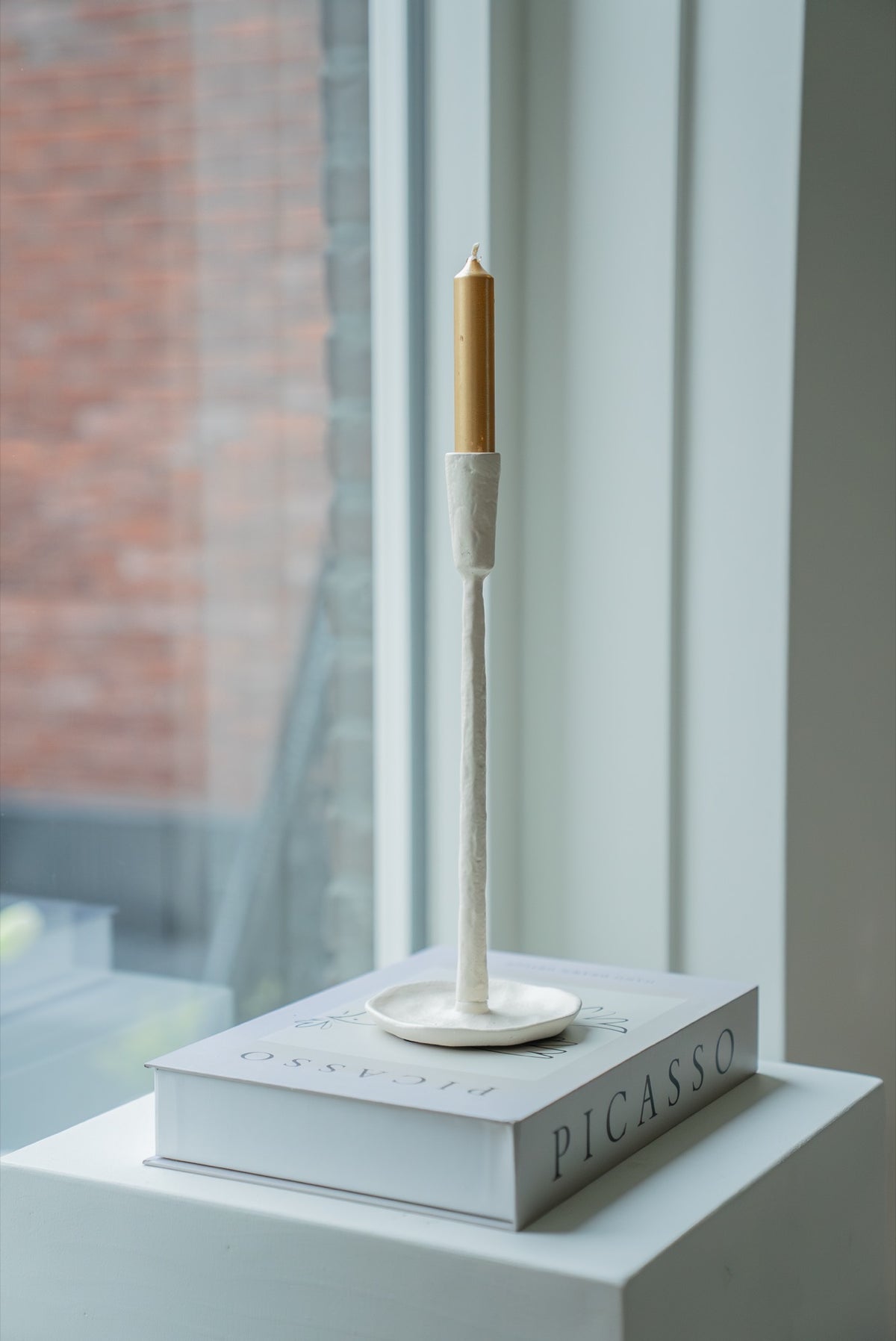 Gebroken witte kandelaar met gouden kaars op een boekenstapel bij het raam