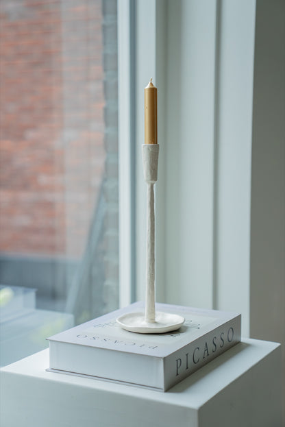 Gebroken witte kandelaar met gouden kaars op een boekenstapel bij het raam