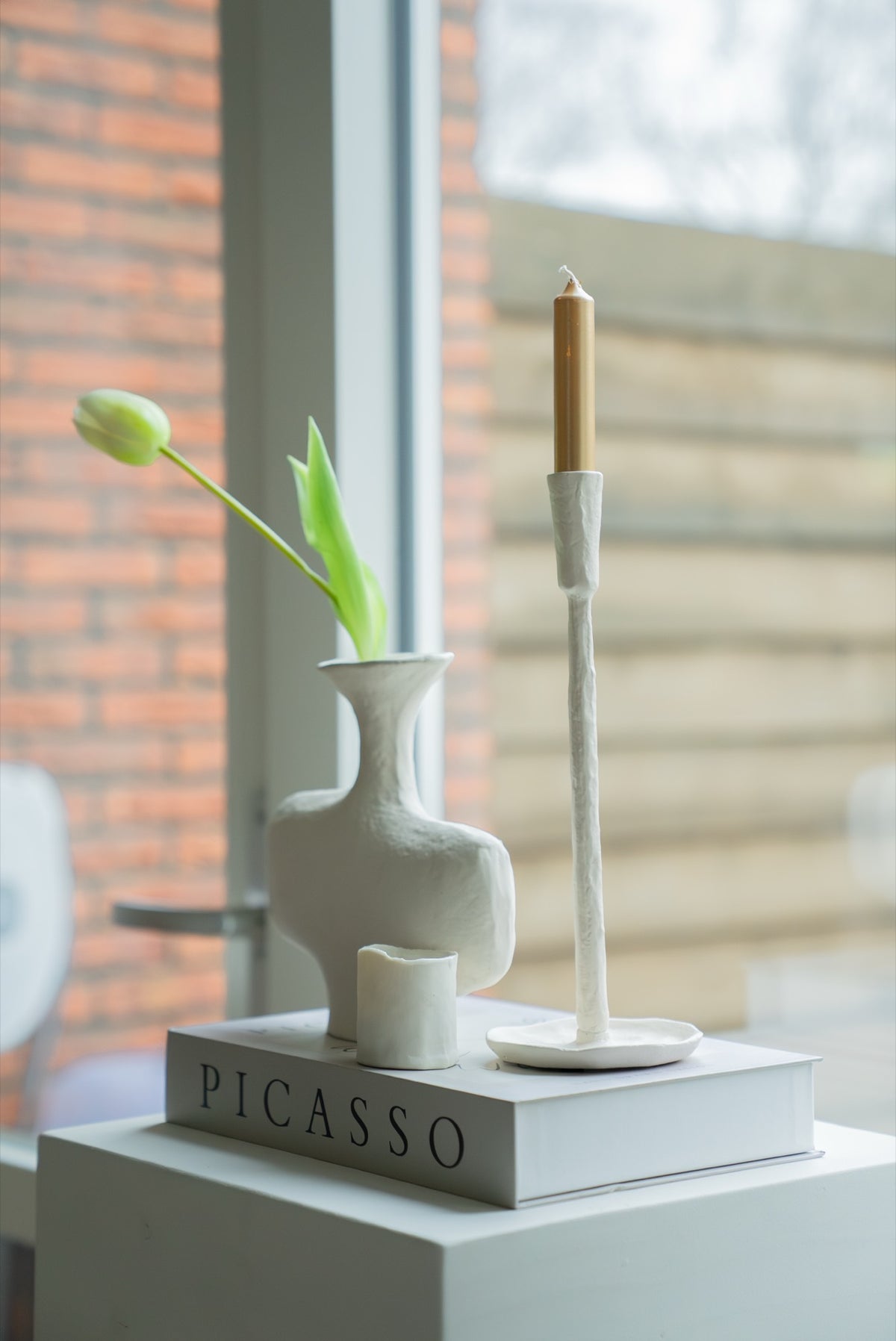 Gebroken witte kandelaar naast een witte vaas met tulp bij het raam