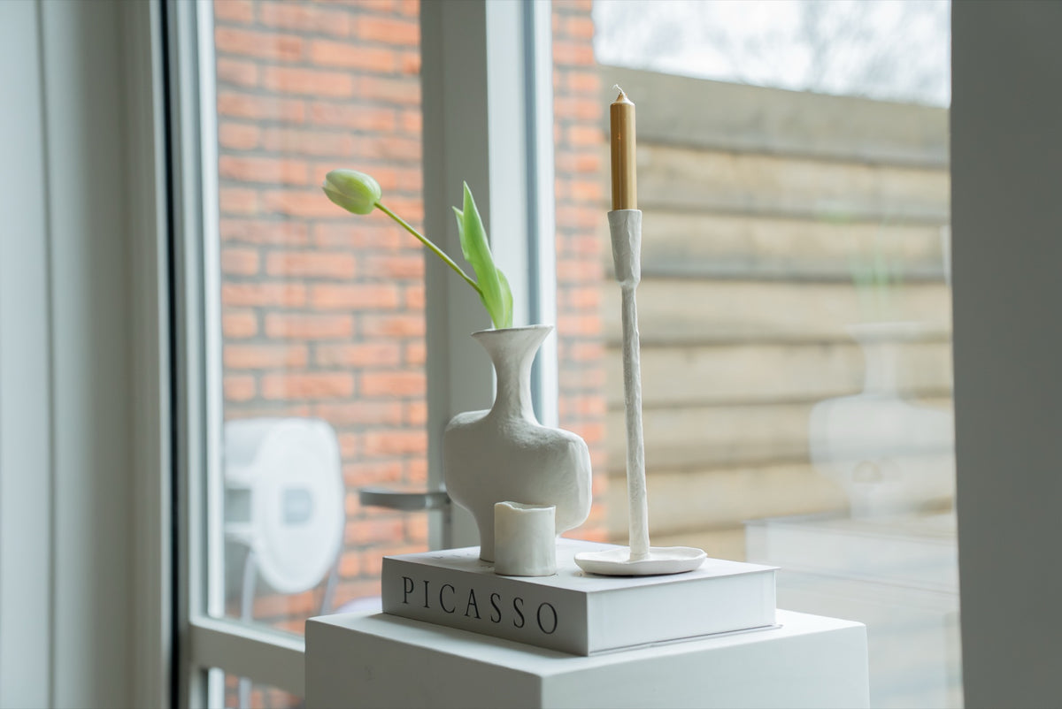 Gebroken witte vaas met tulp en witte kandelaar bij het raam