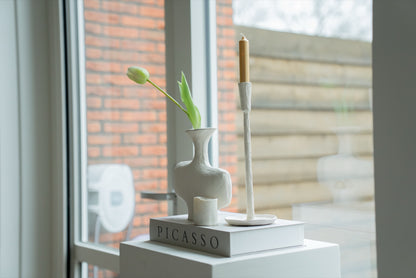 Gebroken witte vaas met tulp en witte kandelaar bij het raam